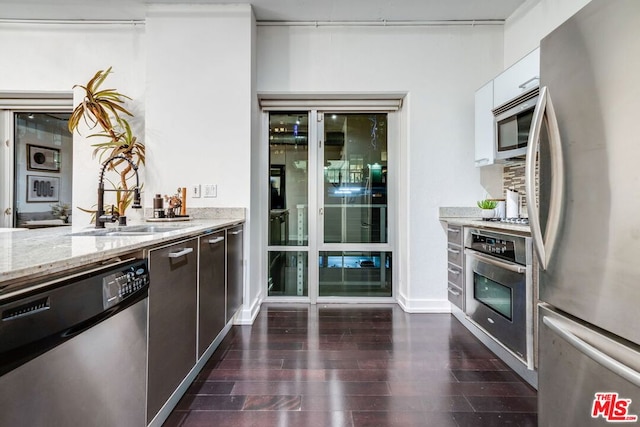 kitchen with light stone countertops, dark hardwood / wood-style floors, stainless steel appliances, white cabinetry, and dark brown cabinets