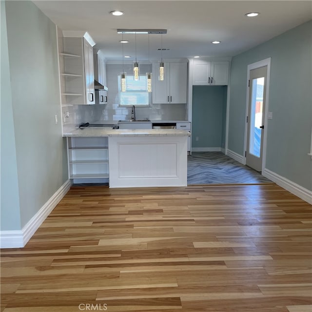 kitchen featuring kitchen peninsula, white cabinets, decorative light fixtures, and light wood-type flooring