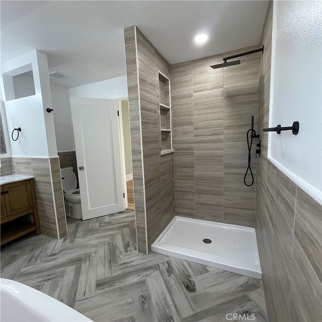 bathroom with vanity, toilet, a tile shower, and tile walls