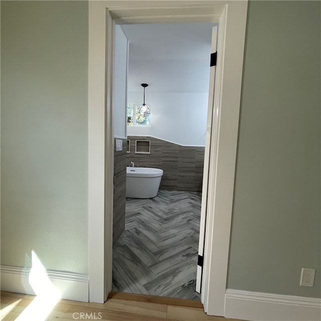 bathroom with tile walls, a bathtub, and wood-type flooring