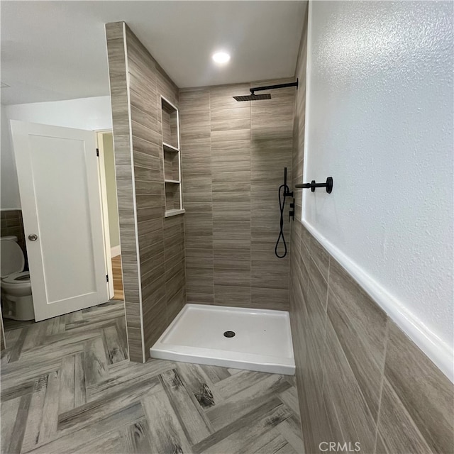 bathroom with tile walls, a tile shower, and toilet