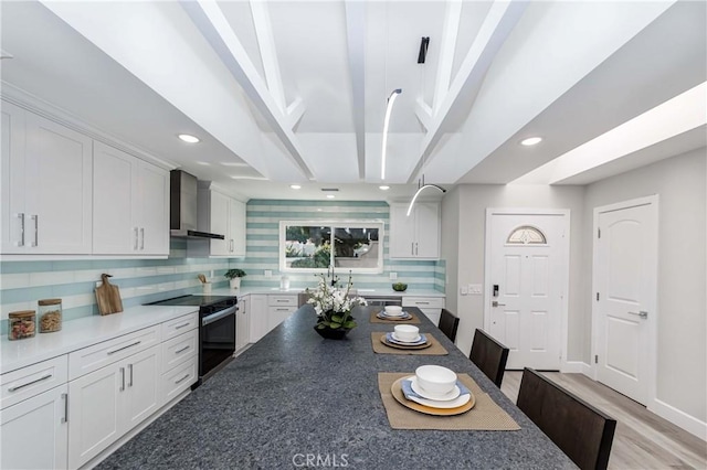 kitchen featuring wall chimney exhaust hood, stainless steel electric range, and white cabinetry