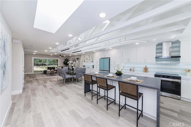 kitchen featuring appliances with stainless steel finishes, light wood-type flooring, wall chimney exhaust hood, white cabinets, and a center island