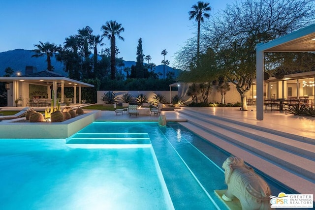 pool at dusk with a gazebo, a patio area, and a mountain view