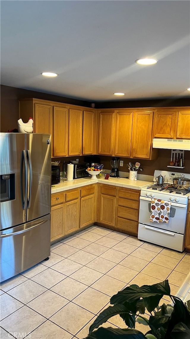 kitchen with light tile patterned flooring, white range with gas cooktop, and stainless steel refrigerator with ice dispenser