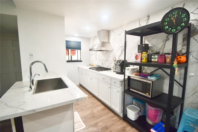 kitchen with wall chimney range hood, sink, light wood-type flooring, appliances with stainless steel finishes, and white cabinets