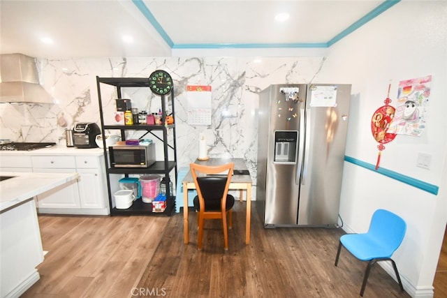 kitchen featuring wall chimney range hood, white cabinets, appliances with stainless steel finishes, hardwood / wood-style flooring, and ornamental molding