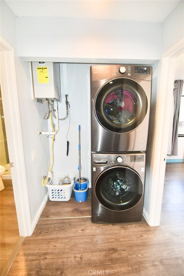 laundry room featuring stacked washer / dryer, wood-type flooring, and tankless water heater