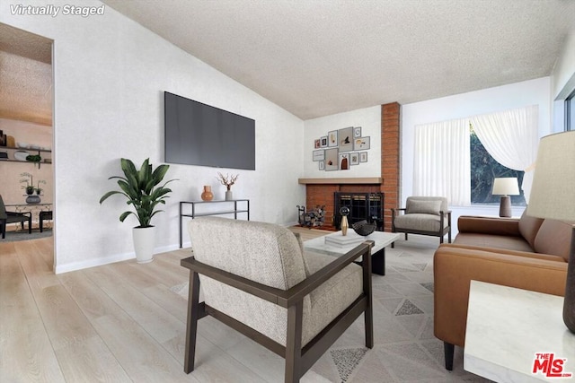 living room featuring vaulted ceiling, a brick fireplace, a textured ceiling, and light wood-type flooring