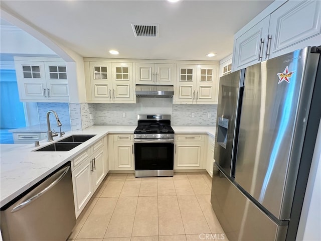 kitchen with light tile patterned floors, sink, stainless steel appliances, light stone countertops, and decorative backsplash