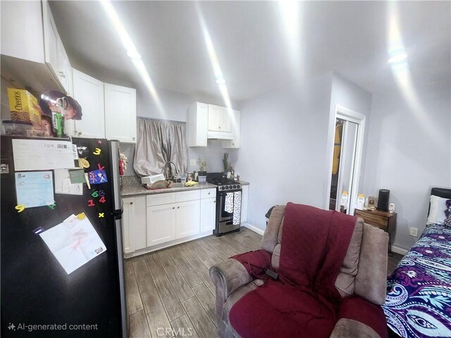 kitchen with stove, light wood-type flooring, light stone counters, white cabinetry, and stainless steel refrigerator