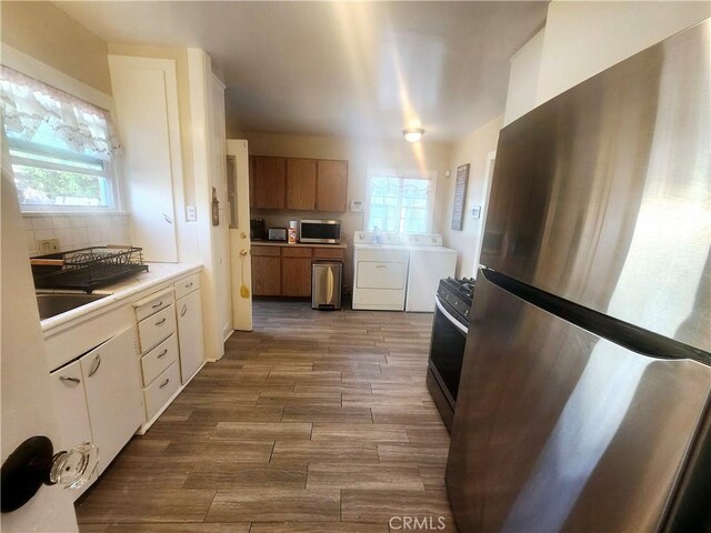 kitchen featuring hardwood / wood-style flooring, plenty of natural light, washer and clothes dryer, and appliances with stainless steel finishes