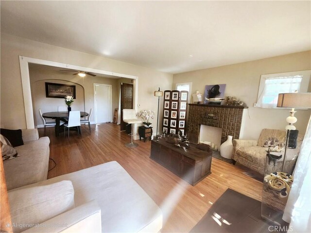 living room featuring hardwood / wood-style floors, ceiling fan, and a brick fireplace