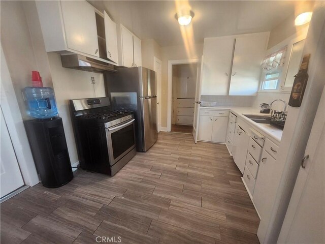 kitchen with appliances with stainless steel finishes, exhaust hood, sink, light hardwood / wood-style flooring, and white cabinets