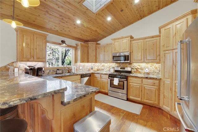 kitchen with a kitchen breakfast bar, kitchen peninsula, lofted ceiling with skylight, pendant lighting, and appliances with stainless steel finishes