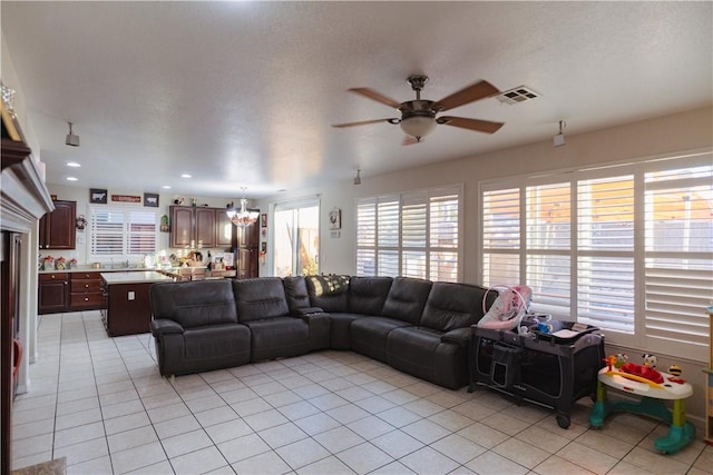 living room featuring a textured ceiling, light tile patterned floors, and ceiling fan with notable chandelier