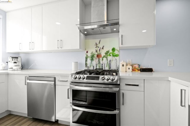 kitchen with stainless steel appliances, wall chimney range hood, dark hardwood / wood-style floors, and white cabinets