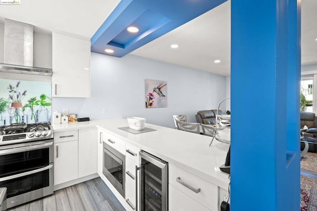 kitchen with wall chimney exhaust hood, white cabinetry, beverage cooler, appliances with stainless steel finishes, and light hardwood / wood-style floors