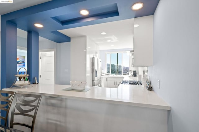 kitchen with sink, a raised ceiling, kitchen peninsula, white cabinets, and stainless steel refrigerator with ice dispenser