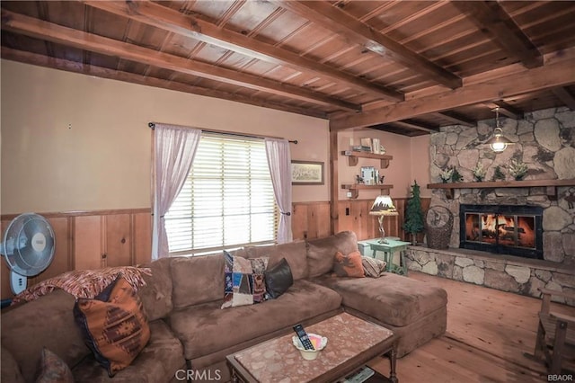 living room featuring wooden walls, beam ceiling, wood-type flooring, wooden ceiling, and a stone fireplace