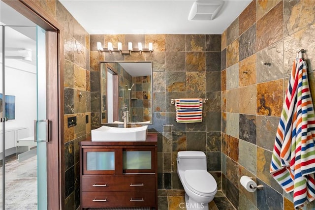 bathroom with vanity, toilet, a shower with shower door, and tile walls