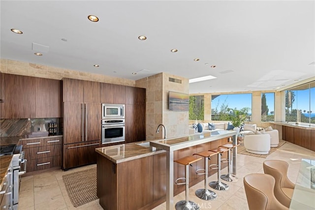 kitchen featuring a large island, sink, light tile patterned floors, built in appliances, and tasteful backsplash