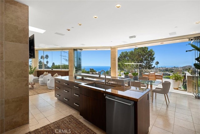 kitchen with a healthy amount of sunlight, dishwasher, an island with sink, sink, and dark brown cabinets