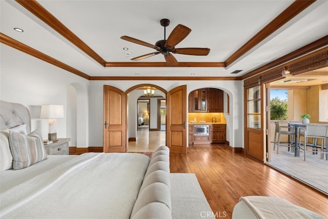 bedroom with crown molding, a tray ceiling, and light wood-type flooring