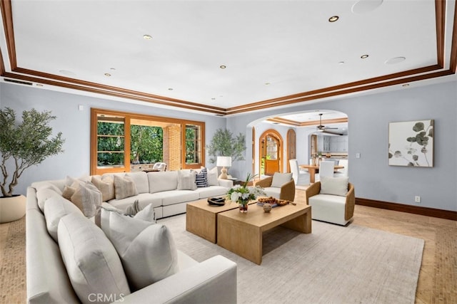 living room with ceiling fan, a raised ceiling, and ornamental molding