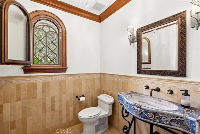 bathroom with toilet, ornamental molding, and tile walls