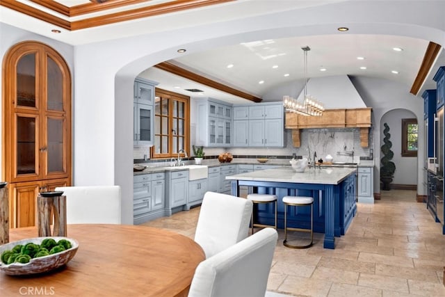 kitchen with hanging light fixtures, backsplash, an inviting chandelier, a kitchen island with sink, and ornamental molding