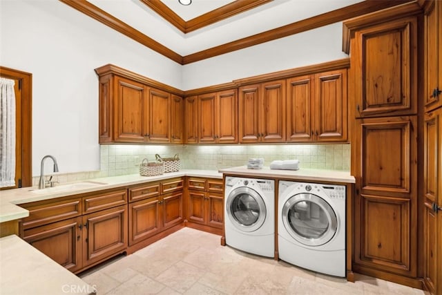 clothes washing area featuring cabinets, crown molding, sink, and washing machine and clothes dryer