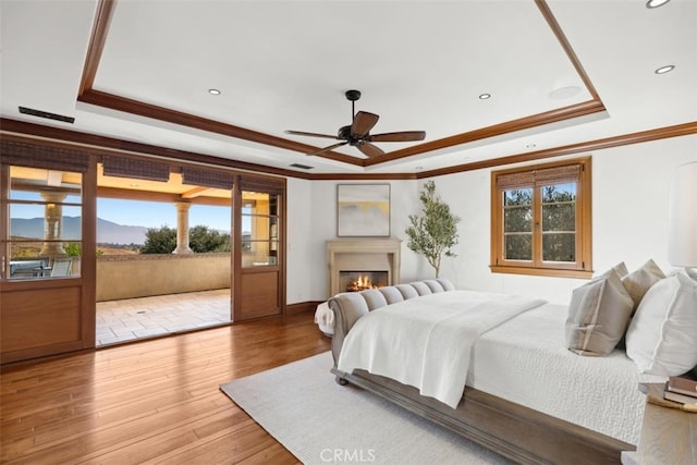 bedroom with ceiling fan, a raised ceiling, wood-type flooring, and a mountain view