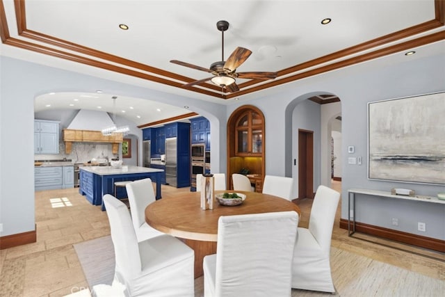 dining room featuring a raised ceiling, ornamental molding, and ceiling fan with notable chandelier