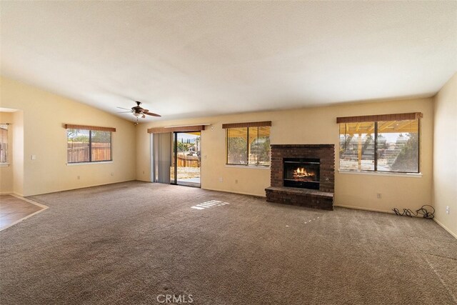 unfurnished living room with ceiling fan, lofted ceiling, carpet flooring, and a brick fireplace