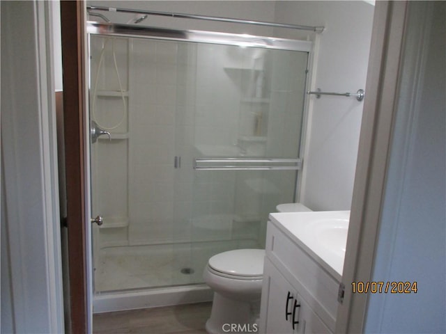 bathroom featuring a shower with door, vanity, hardwood / wood-style floors, and toilet