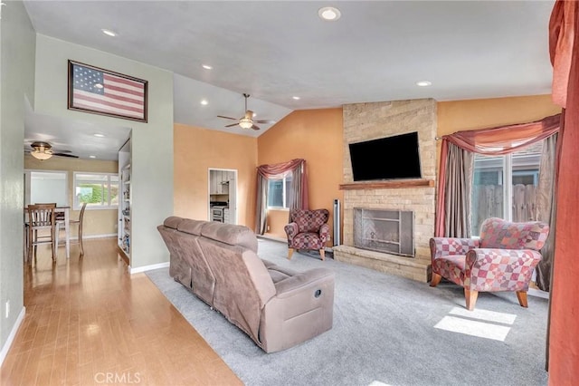 living room with ceiling fan, a stone fireplace, light hardwood / wood-style flooring, and vaulted ceiling