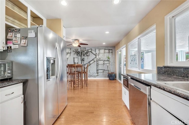 kitchen featuring ceiling fan, stainless steel appliances, light hardwood / wood-style flooring, dark stone countertops, and white cabinets