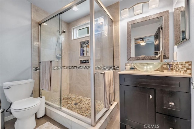 bathroom with backsplash, vanity, ceiling fan, toilet, and a shower with shower door