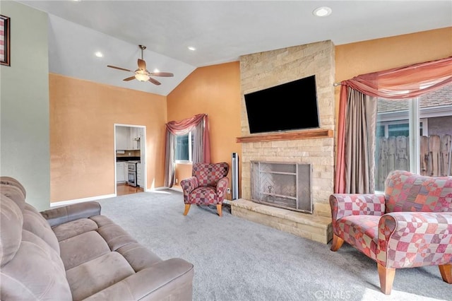 living room with carpet flooring, vaulted ceiling, ceiling fan, and a stone fireplace