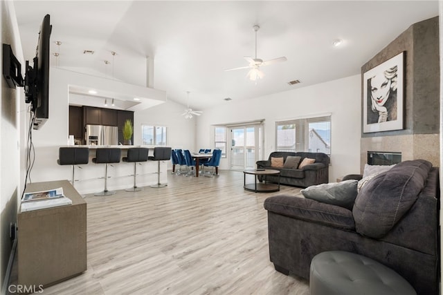 living room with light hardwood / wood-style floors, a tile fireplace, vaulted ceiling, and ceiling fan