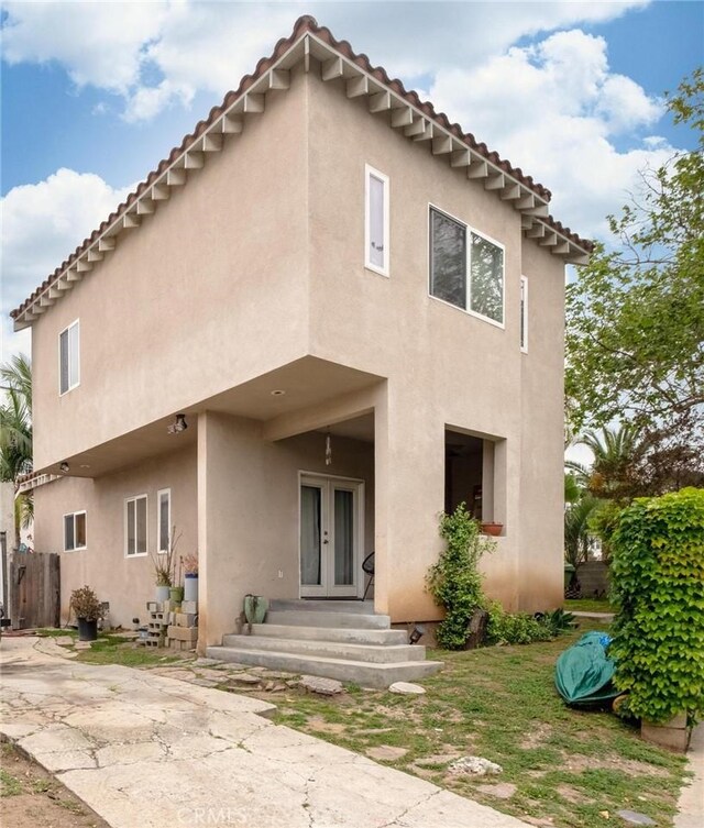 rear view of house with a tile roof, fence, stucco siding, and french doors