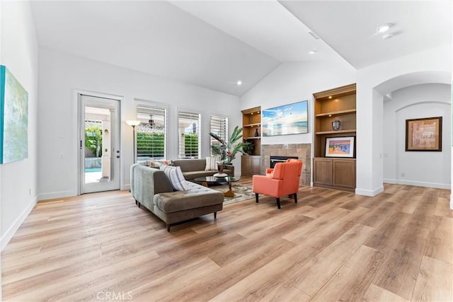 living area featuring a tiled fireplace, high vaulted ceiling, and light wood-type flooring