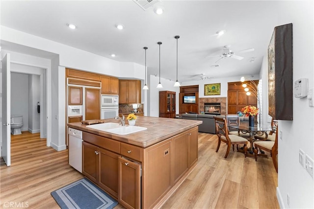 kitchen with pendant lighting, sink, white appliances, light hardwood / wood-style flooring, and a kitchen island with sink