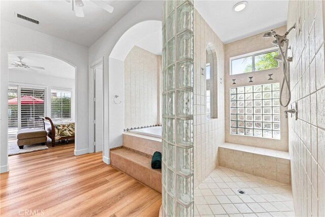 bathroom featuring a healthy amount of sunlight, ceiling fan, hardwood / wood-style flooring, and tiled shower