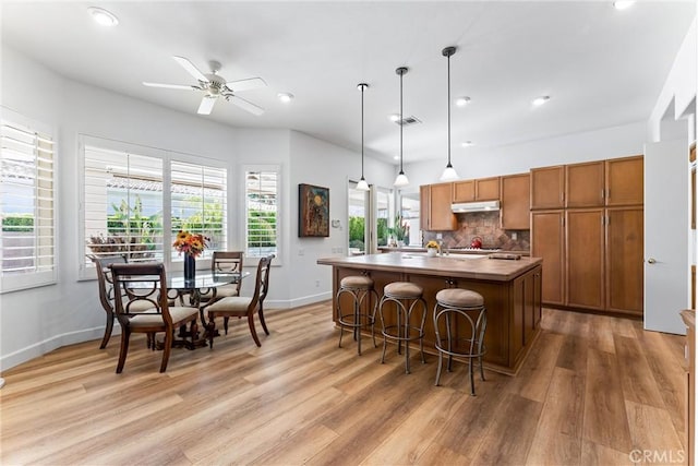 kitchen with an island with sink, pendant lighting, backsplash, and light wood-type flooring