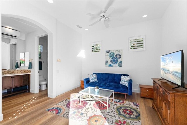 living room with ceiling fan, plenty of natural light, a wall unit AC, and light hardwood / wood-style flooring