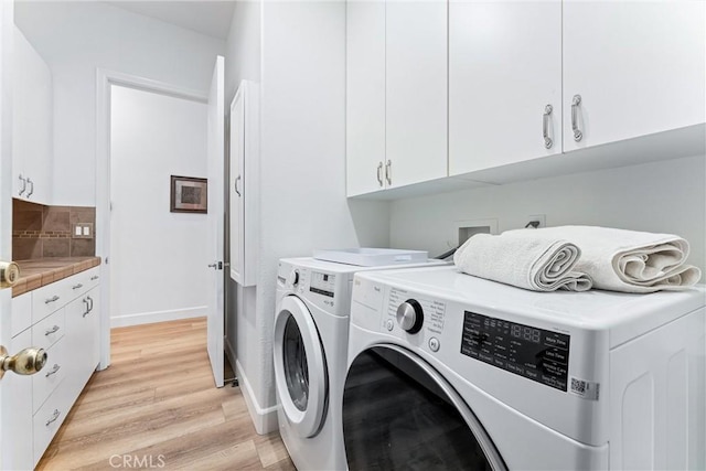 clothes washing area featuring cabinets, washing machine and dryer, and light hardwood / wood-style floors