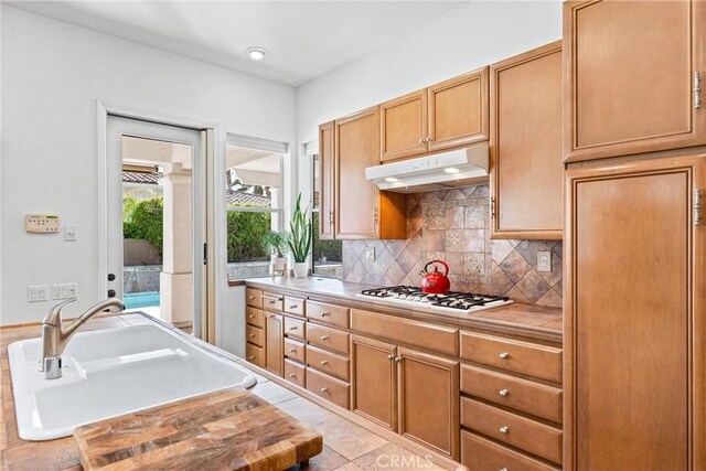 kitchen with butcher block countertops, sink, light tile patterned floors, backsplash, and gas stovetop