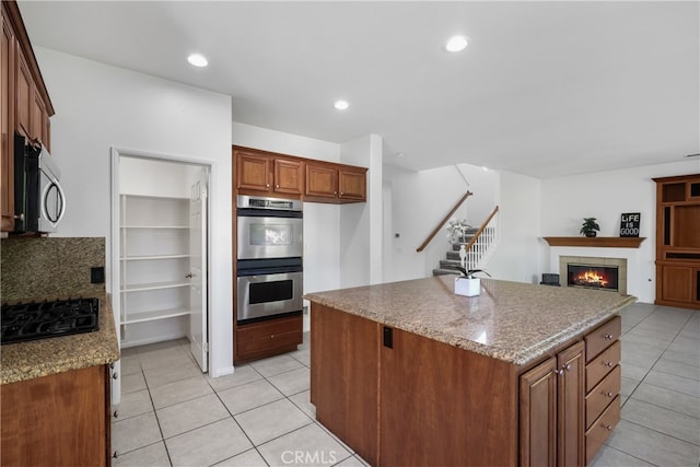 kitchen featuring appliances with stainless steel finishes, light stone counters, a tiled fireplace, and light tile patterned floors